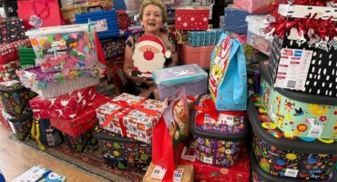 An elderly woman holding a Santa Clause gift surrounded by gifts.