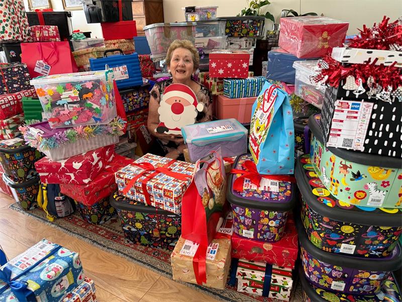 An elderly woman holding a Santa Clause gift surrounded by gifts.
