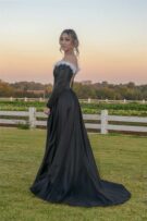 Girl in a black dress with white detailing standing in front white fence at sunset
