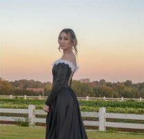 Girl in a black dress with white detailing standing in front white fence at sunset
