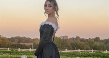 Girl in a black dress with white detailing standing in front white fence at sunset