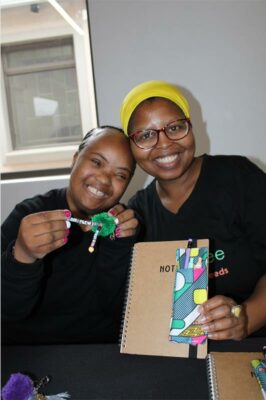 A black girl sitting with a black woman wearing a yellow bandana