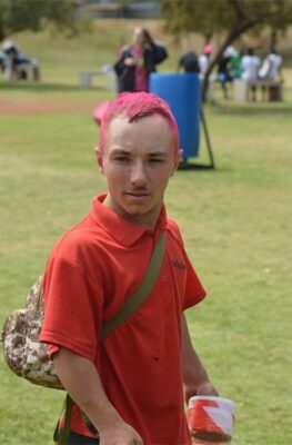 Boy with hair sprayed pink walks holding caution tape in his hand.