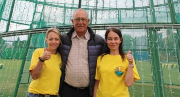 Two women and a man standing in front of green mesh.