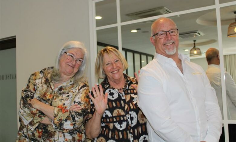 A man and woman stand with their arms crossed with the woman in the middle smiling with her hands up.