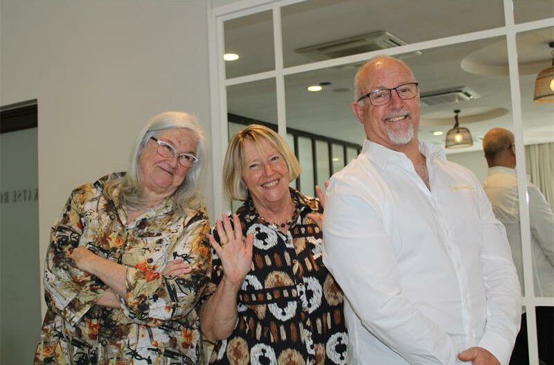 A man and woman stand with their arms crossed with the woman in the middle smiling with her hands up.