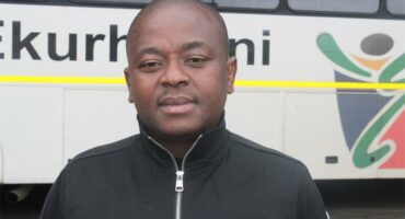 MMC of Roads and Transport Management, Andile Mngwevu, with a white municipal bus in the background.