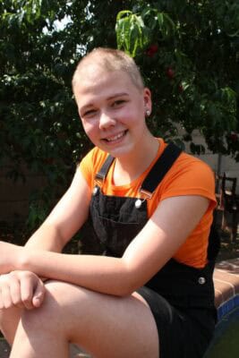 Girl wearing an orange top and black dress with no hair