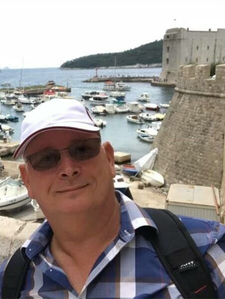 Man with white cap and sunglasses with boats in the background.