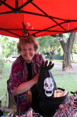 An older woman with a plastic nose, dressed as a witch standing under an orange gazebo