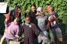 Five children dressed in Halloween costumes and a man dressed in a black cape and green mask