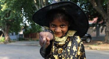Indian girl dressed as a witch points a wand at the camera