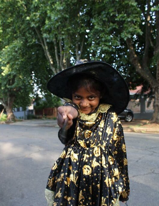 Indian girl dressed as a witch points a wand at the camera