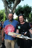 Man with a blue shirt and a red analog clock hanging from his neck a woman holding a cricket bat