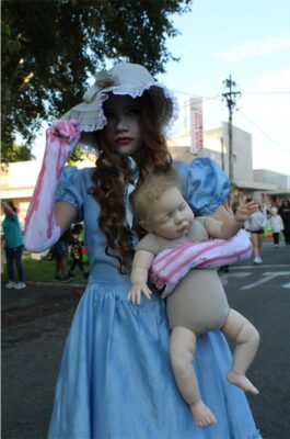 A girl in a white bonnet and blue dress holding a doll