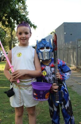 A girl in white with purple lightning bolts on her face with a boy dressed as a blue autobot