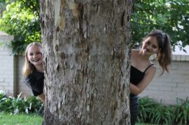 Two girls looking out from behind a tree