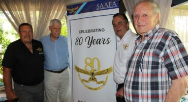 Four elderly men standing in front of a white banner