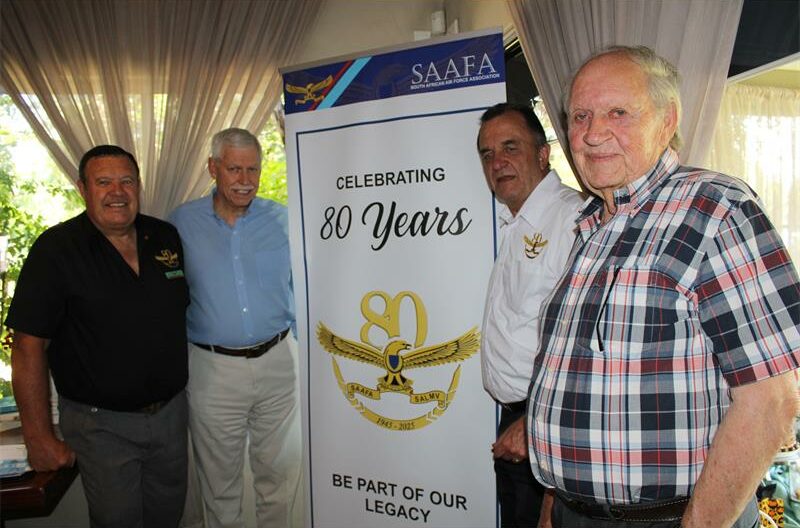 Four elderly men standing in front of a white banner