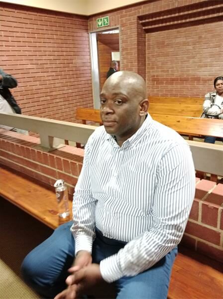 Man sitting in the dock in a court setting with his fingers crossed between his legs