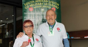 A woman with glasses and a man wearing a white shirt with a Poppy flower printed on the chest