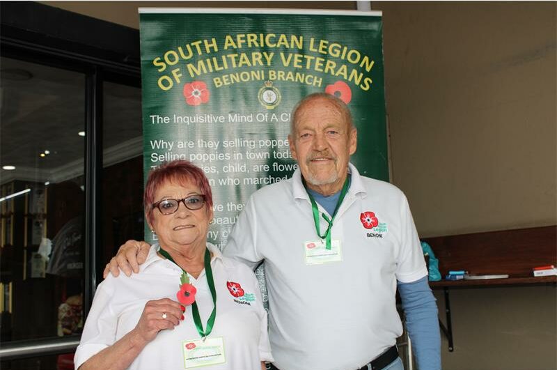A woman with glasses and a man wearing a white shirt with a Poppy flower printed on the chest