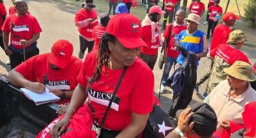 A group of protesters in red union t-shirts marching outside offices.