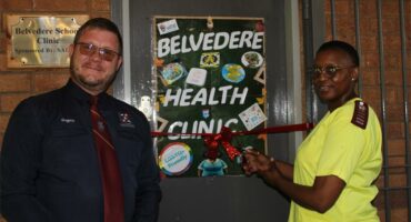 Man with glasses and maroon tie standing next to a woman wearing yellow scrubs.