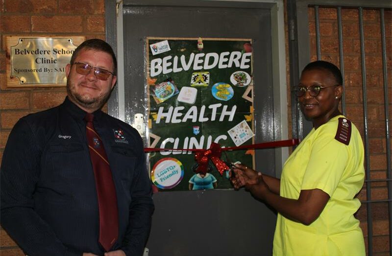 Man with glasses and maroon tie standing next to a woman wearing yellow scrubs.