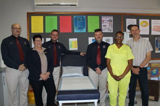 Six people standing next to a hospital bed.