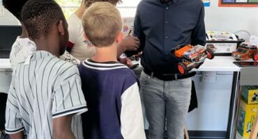 Man with blue cap show four children a robotics vehicle