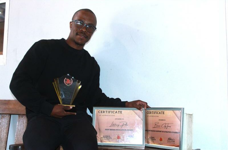 A photo of a man dressed in black. He's carrying a trophy and two certificates.