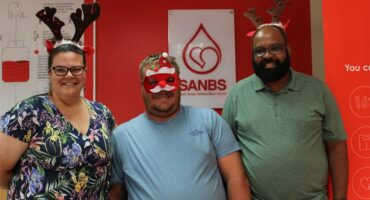 Three people, one woman and two men wearing Christmas costumes.