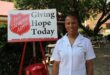 Woman wearing a white overall, standing next to a red and white Salvation Army sign.