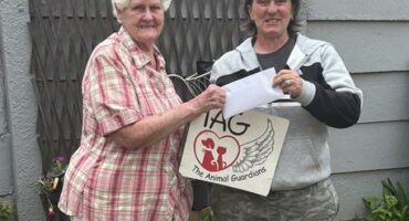 Two women standing in front of a grey wall.