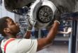 A black man working on a brake drum under a car.