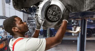 A black man working on a brake drum under a car.