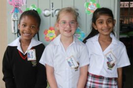 A photo of three Grade One learners from Ashton International College. They are standing in front of a door with different messages and paintings on it.