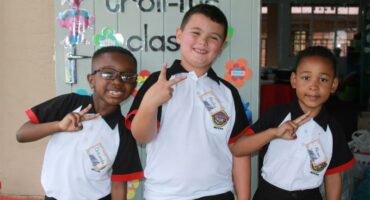 A photo of three Grade One learners from Ashton International College. They are standing in front of a door with different messages and paintings on it.