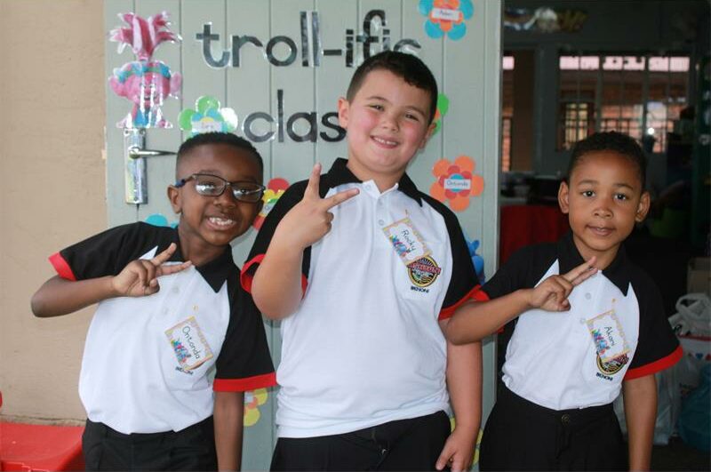 A photo of three Grade One learners from Ashton International College. They are standing in front of a door with different messages and paintings on it.