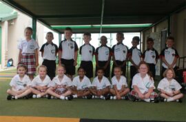 A photo of school children dressed in white shirts, black and white t-shirts. Some are standing while others are sitting down.