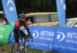 A photo of cyclist riding next a blue banner with the words Retina South Africa.