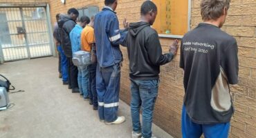 Photo of seven men lined up against a wall.