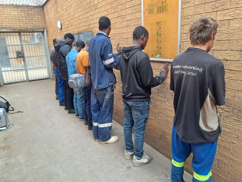 Photo of seven men lined up against a wall.