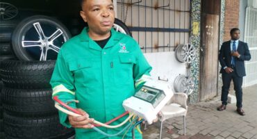 Black man wearing a green overall holding an electrical box