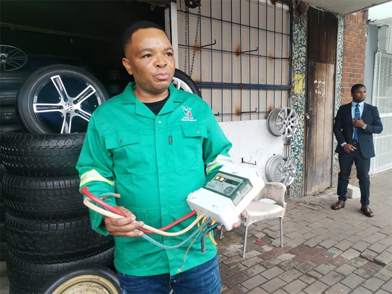 Black man wearing a green overall holding an electrical box