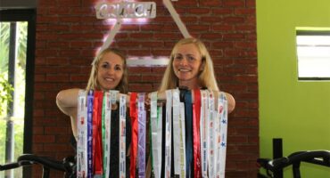 Two blonde women holding medals on their arms
