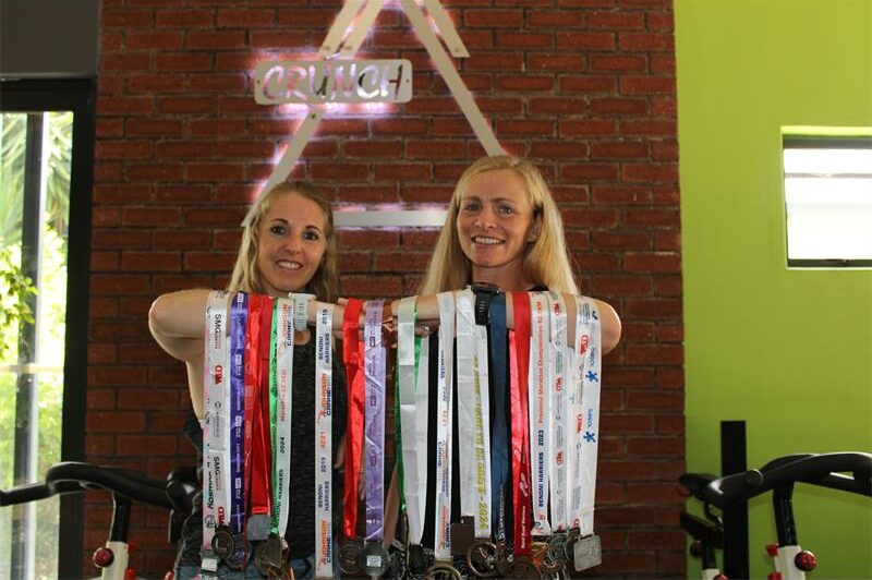 Two blonde women holding medals on their arms
