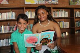 Boy wearing green golf shirt sits with a lady dressed in a Polynesian outfit