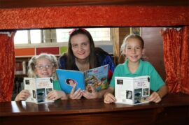 Two girls wearing green gold shirts stand holding books with girl dresses as a fairy princess